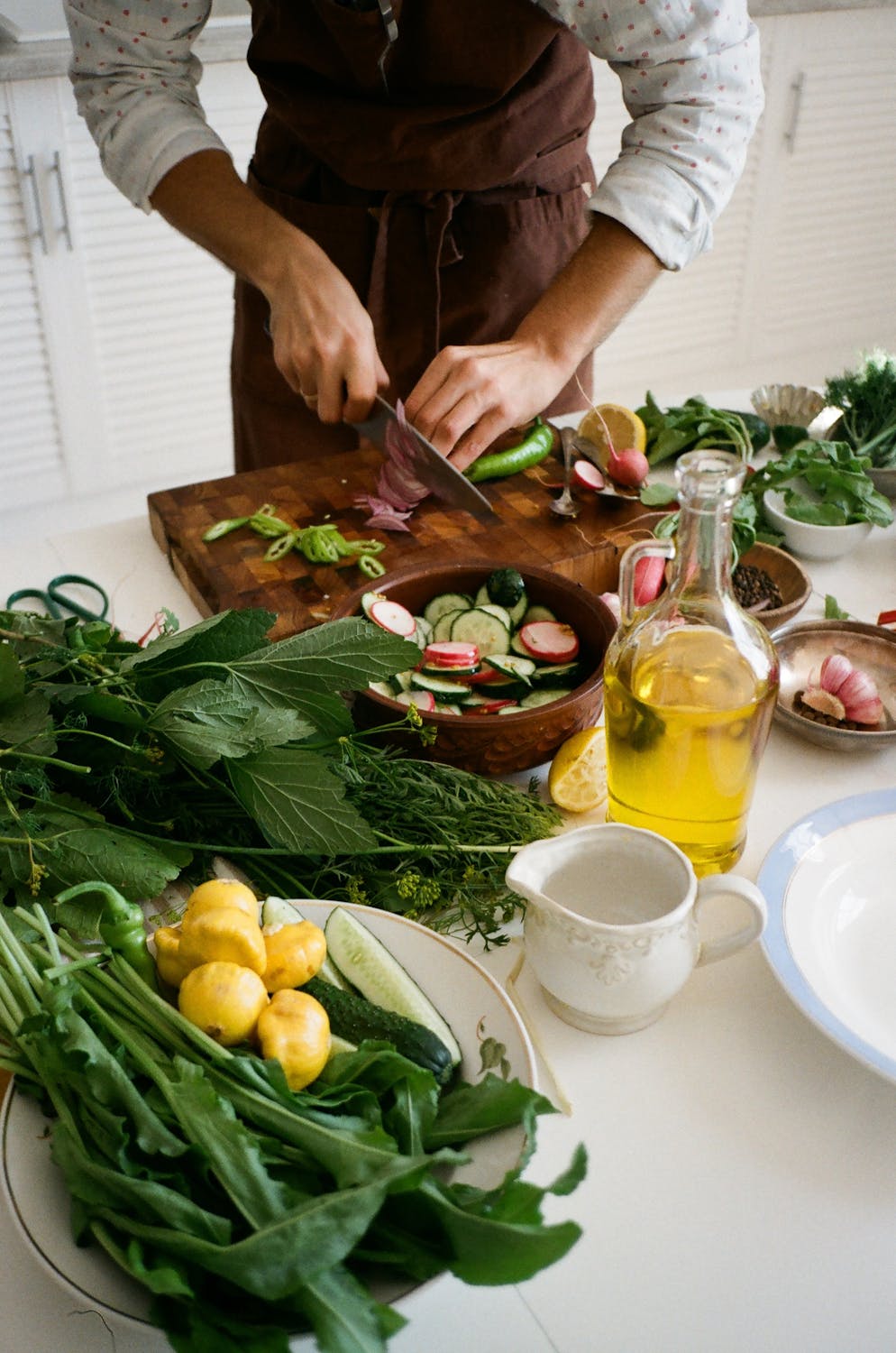 Chef slicing vegetables with a premium kitchen knife on a wooden cutting board surrounded by fresh ingredients and herbs in a modern kitchen.